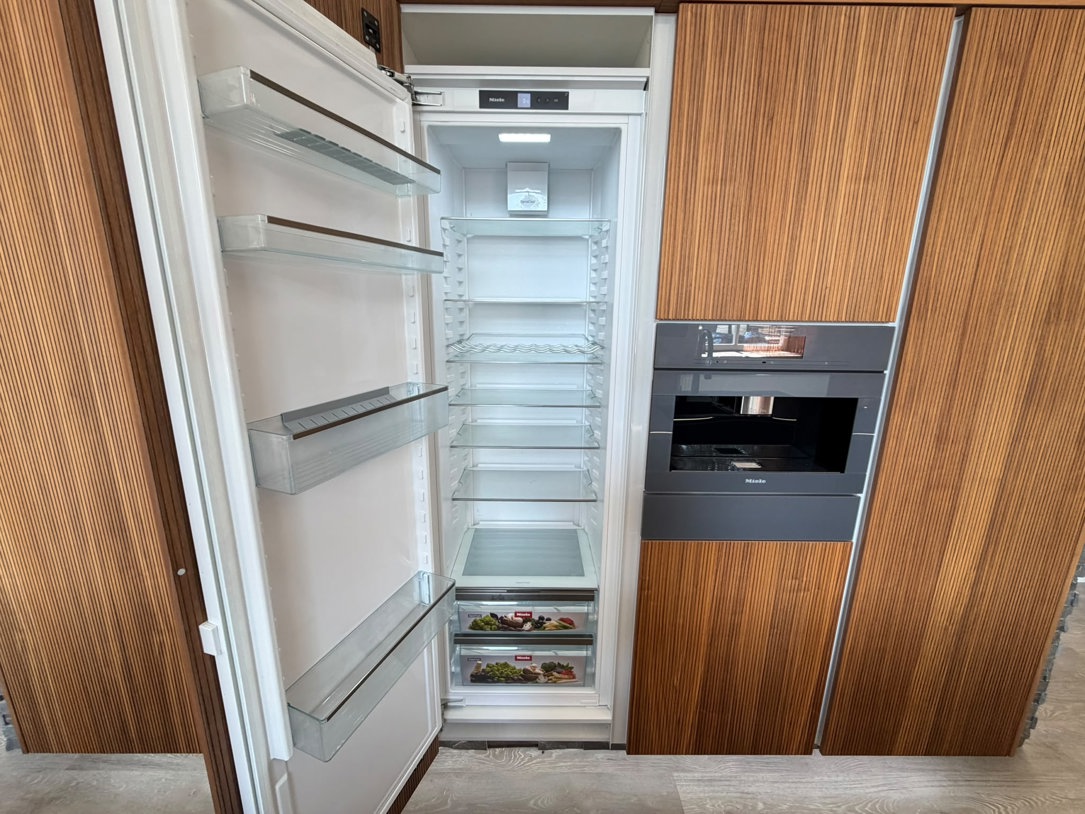 Miele integrated larder fridge with the door open, showing full-height refrigeration behind timber furniture-door cabinetry, Arlington Interiors showroom, Farsley.